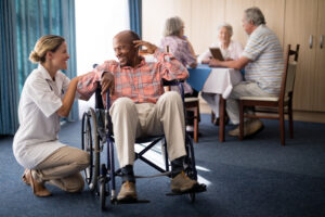 Smiling female doctor kneeling by disabled senior man sitting on wheelchair at retirement home. Myths About Senior Living.